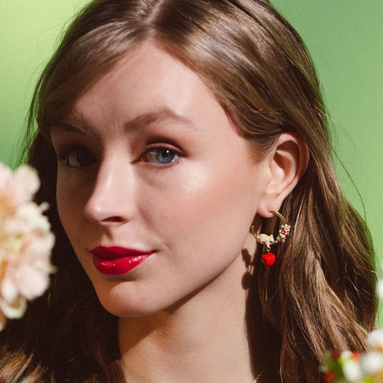Model wearing Apple Blossom & Mouse Hoop Earrings by Bill Skinner, showing dangling red apple detail and gold-plated hoop.