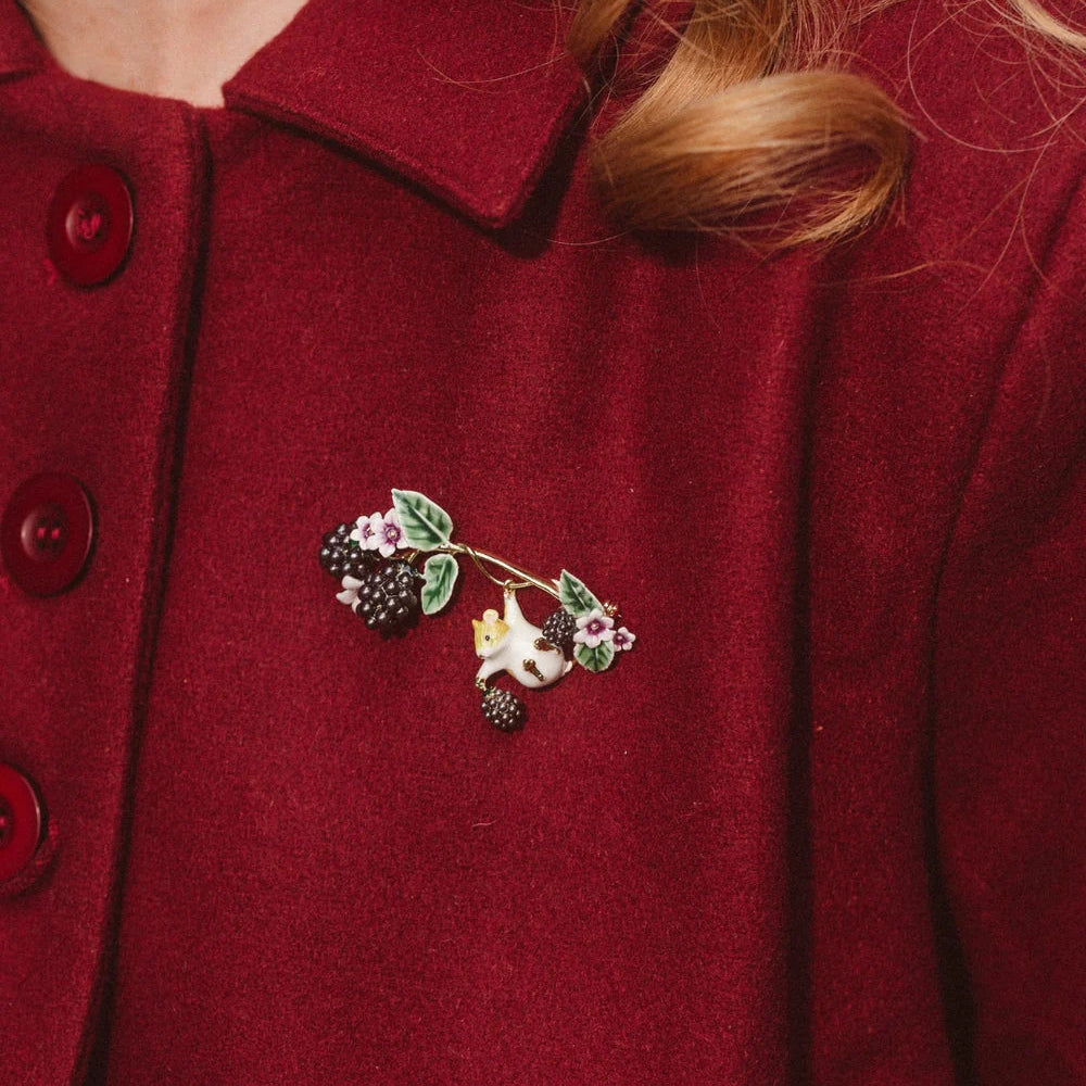 Model wearing Bill Skinner Blackberry & Mouse Brooch pinned to red coat, showing delicate gold-plated enamel design.
