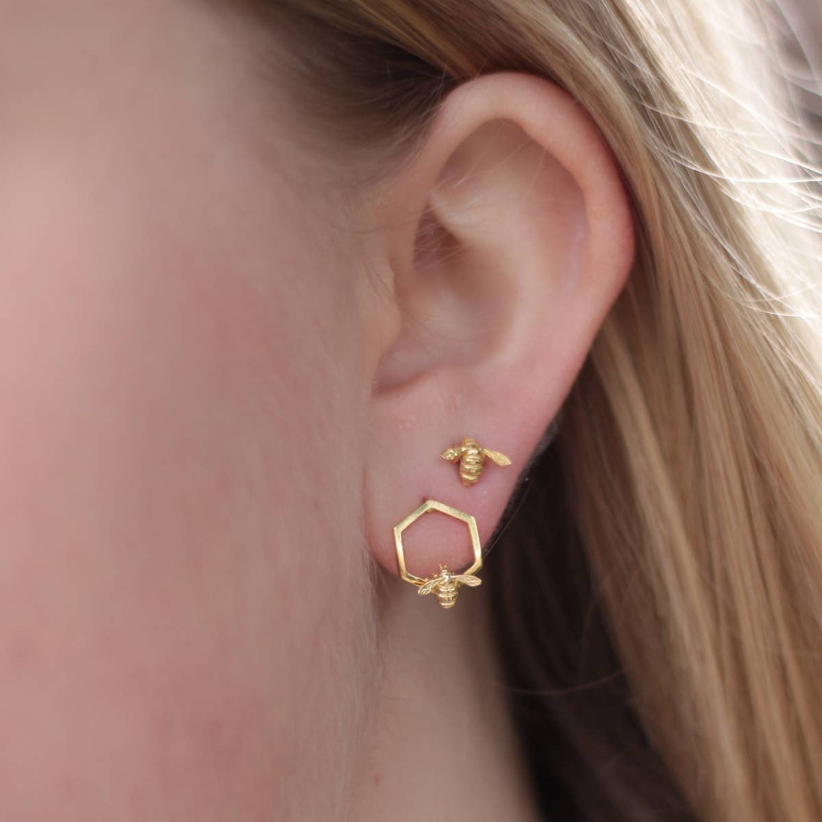 Model wearing Bumble Bee Hex Stud Earrings showing gold bee and honeycomb detail on ear.