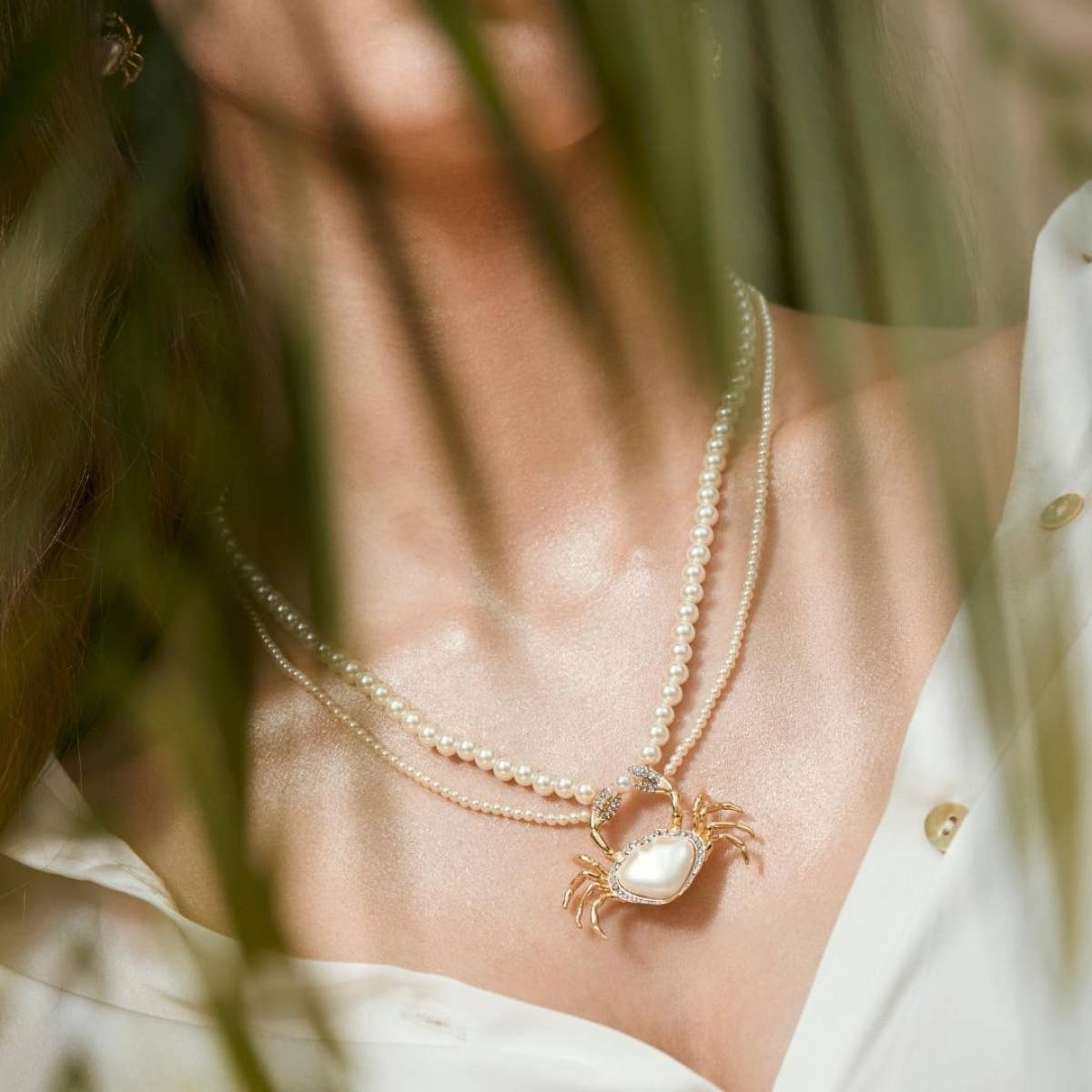 Model wearing Pearly Crab Necklace by Bill Skinner, featuring gold and pearl crab pendant on double pearl strand.