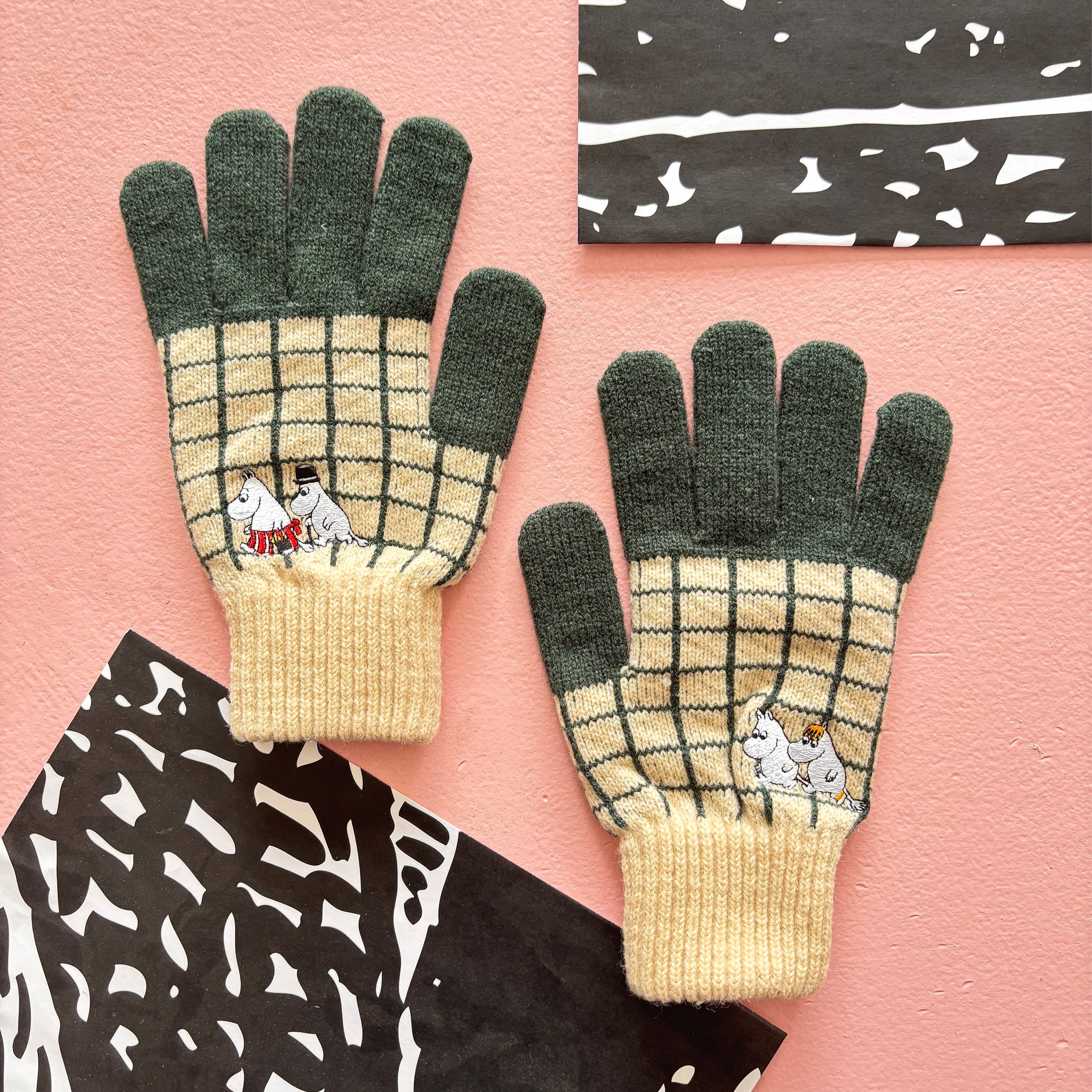 Pair of Moomin Chequered Gloves laid flat on pink background with contrasting black decor.
