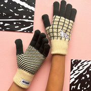 Hands wearing Moomin Chequered Gloves in green and cream knit with embroidered Moomin family design, against pink background.

