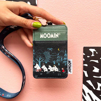 Hand holding Moomin Forest Lanyard with forest design and Moomin characters, against pink background.
