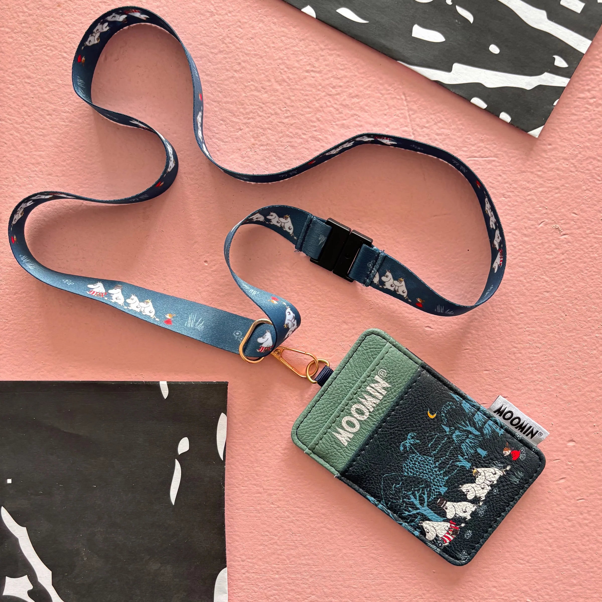 Flat lay of Moomin Forest Lanyard with detachable printed strap on pink background.
