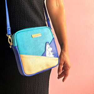 Model wearing Moomin Gold Mini Bag with colour block design in blue, gold, and turquoise.
