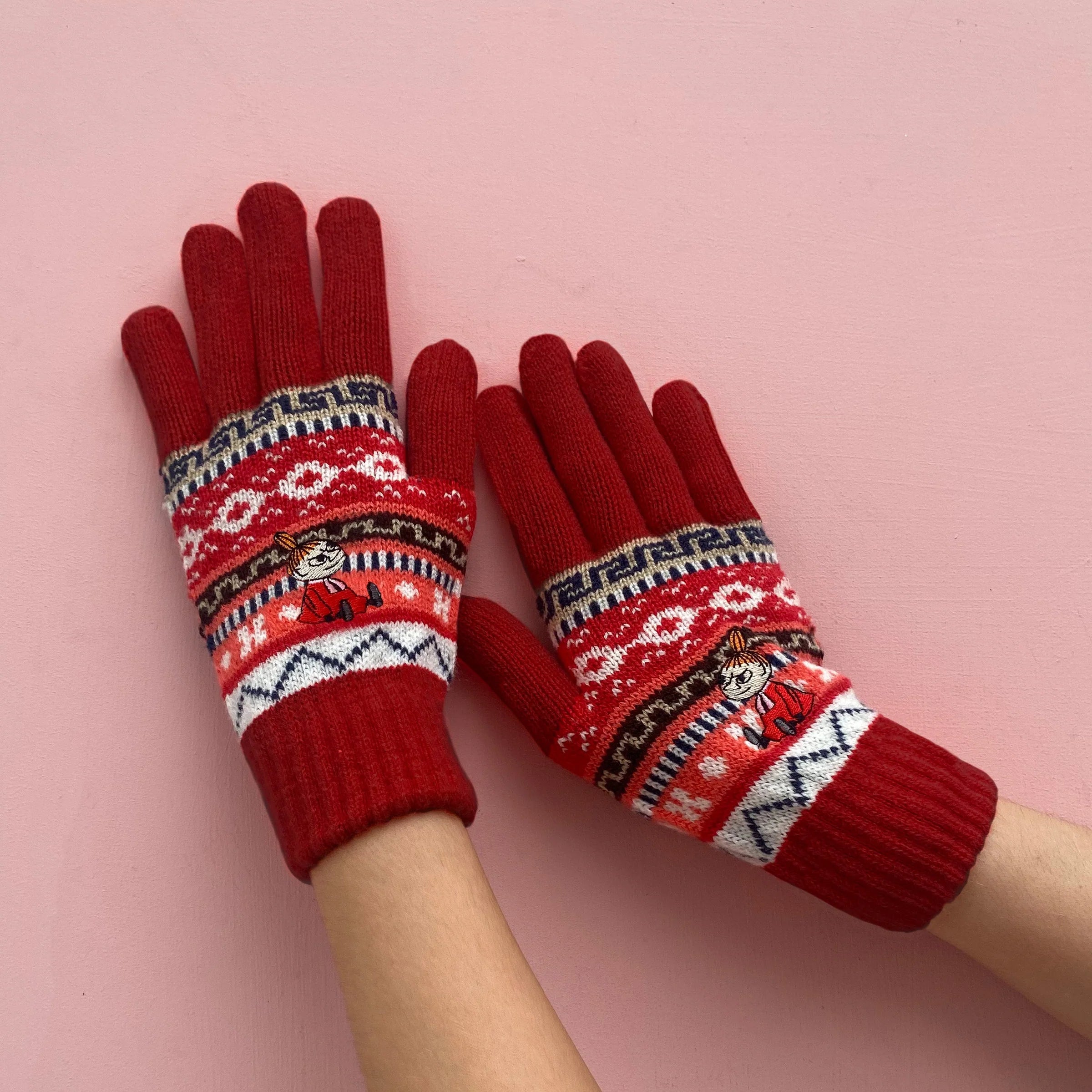 Red Fair Isle Moomin Little My gloves laid flat on pink background.