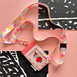 Flat lay of Moomin Little My Lanyard with floral printed strap and pink cardholder on pink background.
