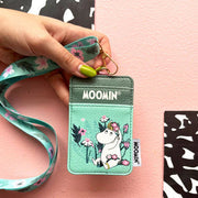 Hand holding Moomin Snorkmaiden Lanyard with floral print and mint green tones on pink background.
