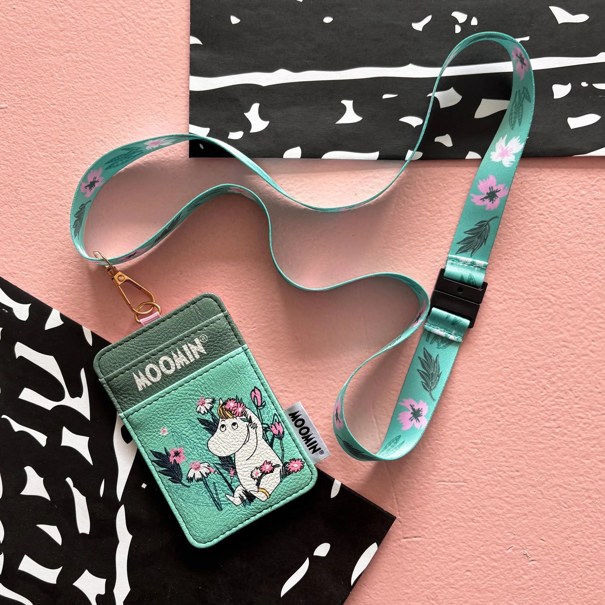 Flat lay of Moomin Snorkmaiden Lanyard with matching floral strap on pink surface.
