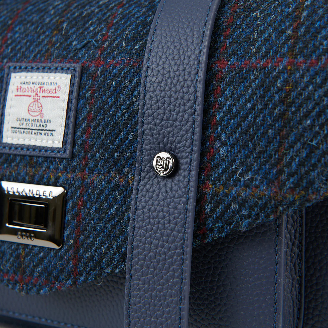 Detail of navy Harris Tweed satchel showing leather strap and metal hardware.