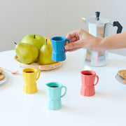 Four ceramic espresso cups with moka pot and coffee being poured