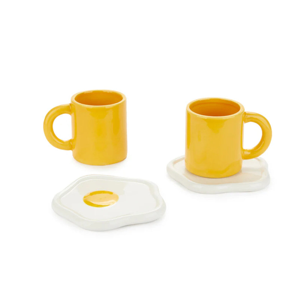 Two yellow cups with fried egg saucers on white background