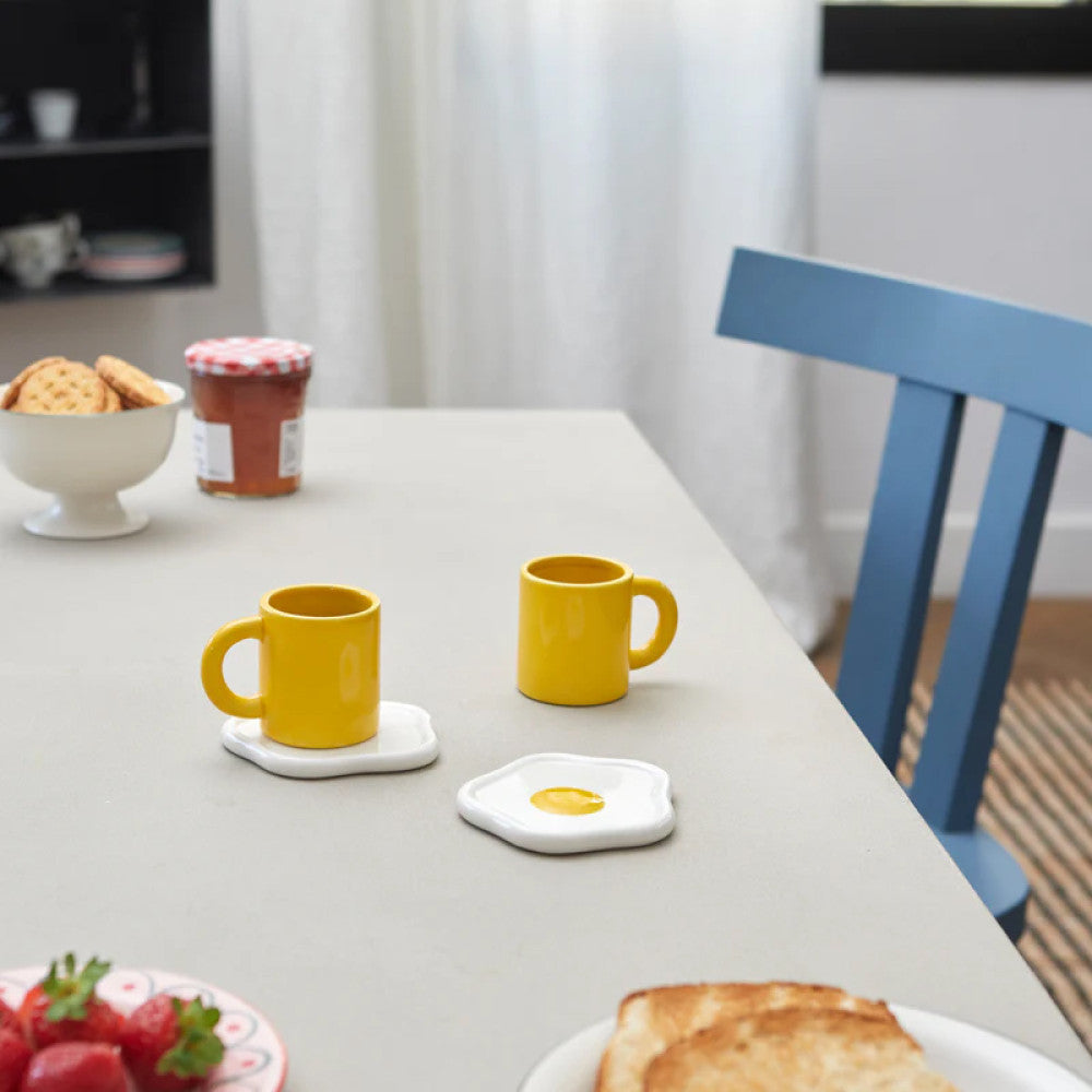 Two yellow cups with fried egg saucers on breakfast table
