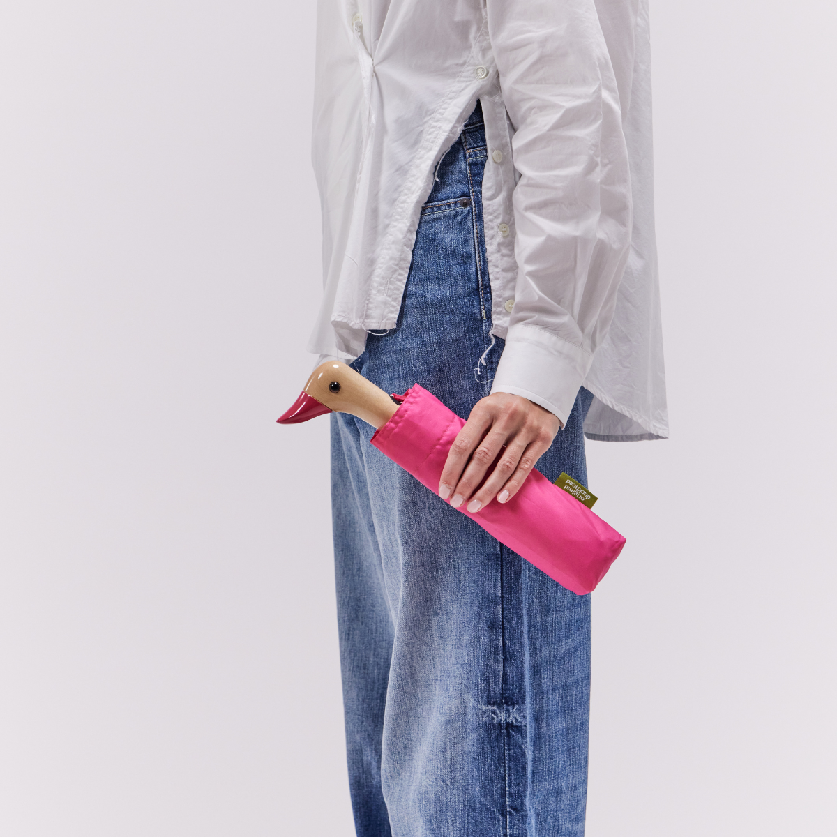 Closed pink compact duck umbrella held in hand lifestyle shot