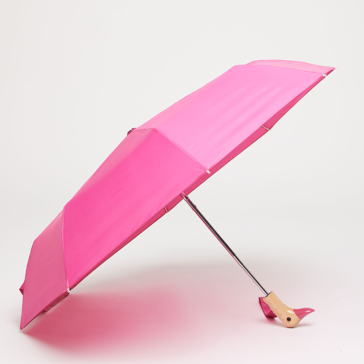 Bonbon pink compact duck umbrella open resting on light grey background