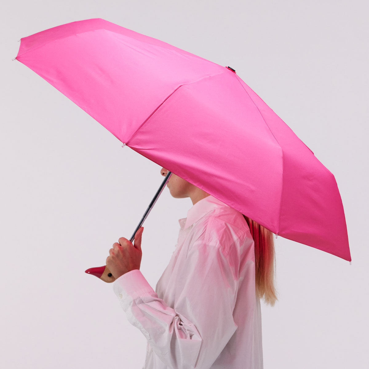 Bonbon pink duck umbrella open held by model side view on grey background