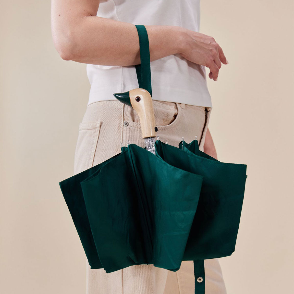 Forest green duck umbrella closed hanging from wrist lifestyle on beige background
