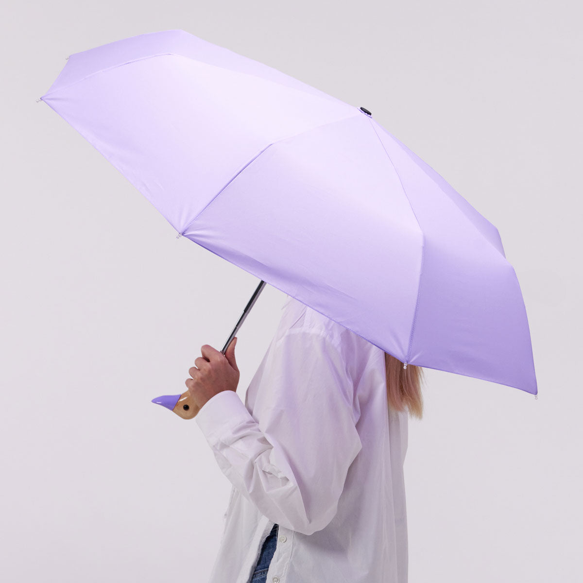 Macaron lilac duck umbrella open held by model side view on grey background