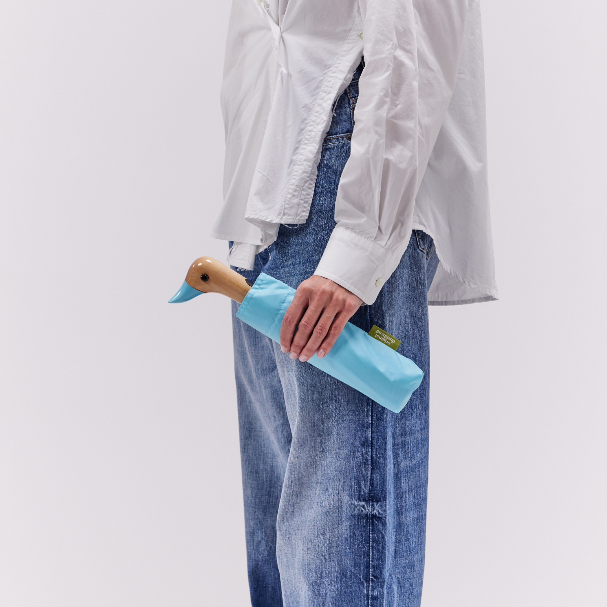 Closed sky blue compact duck umbrella held in hand lifestyle shot