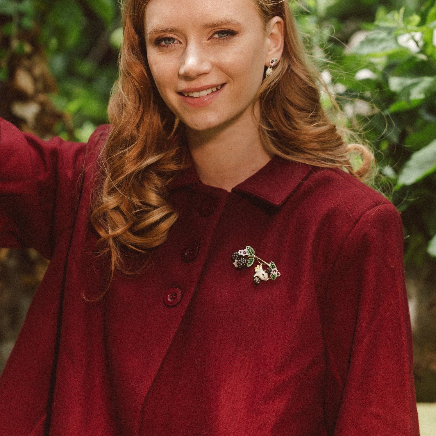 Model outdoors wearing Bill Skinner Blackberry & Mouse Brooch on burgundy coat, part of Blackberry Mouse Collection.