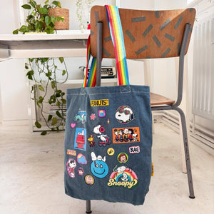 Peanuts patch denim tote bag with rainbow straps on chair