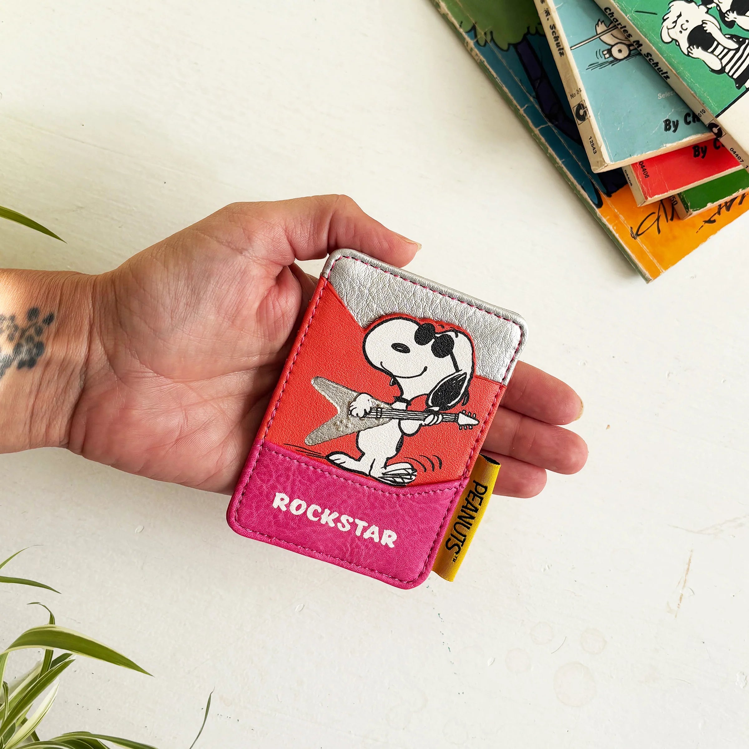 Hand holding Peanuts Rockstar Cardholder with Snoopy illustration and yellow Peanuts tag.