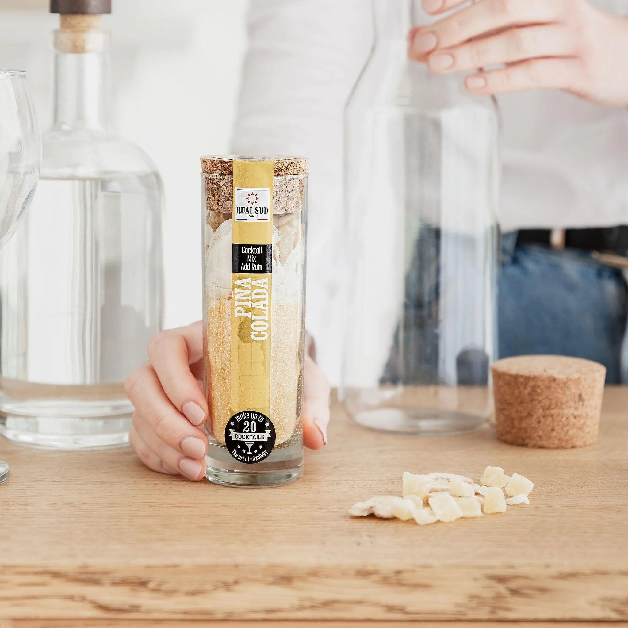 Person preparing Piña Colada cocktail mix with a glass jug and dried pineapple pieces on the table.