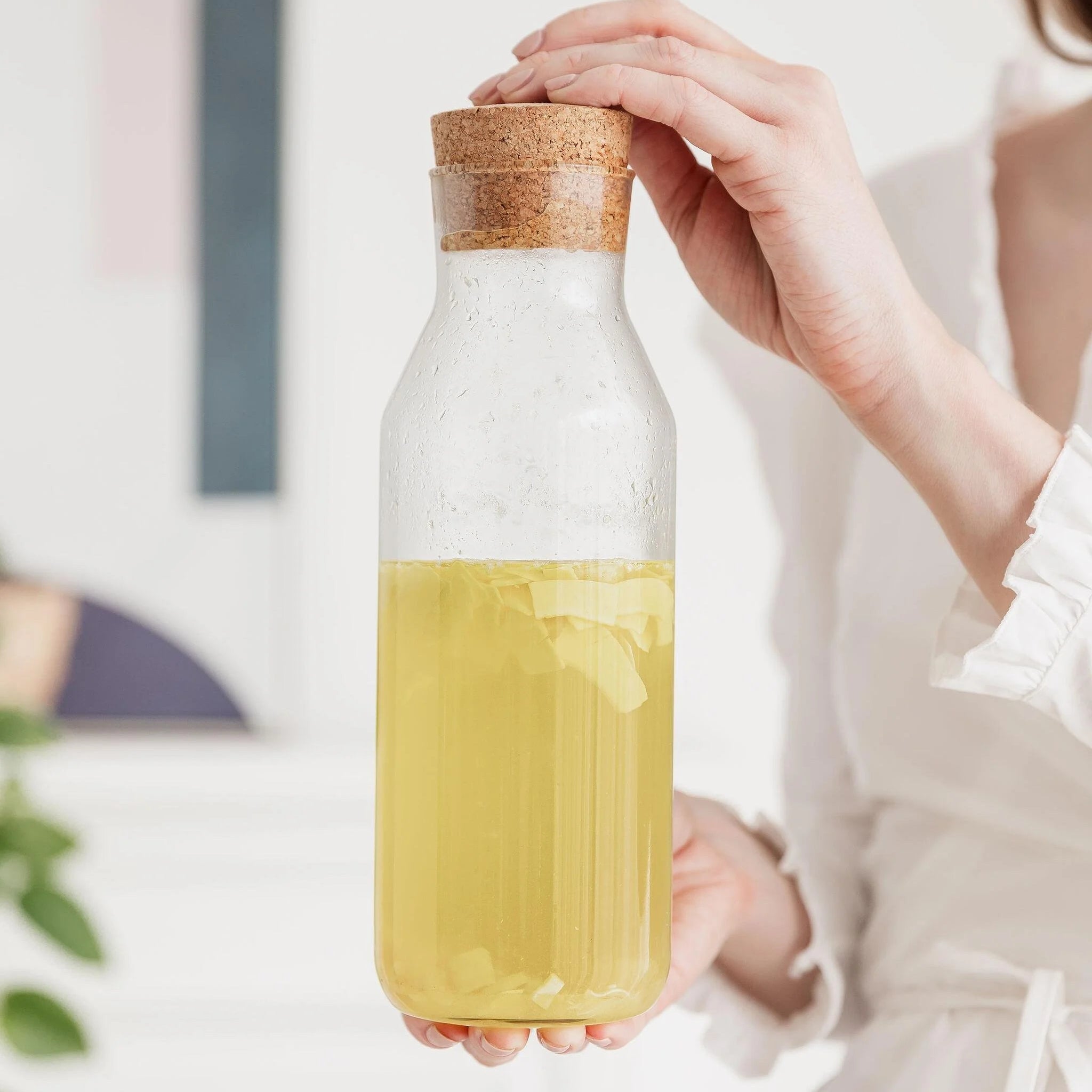 Infused Piña Colada rum mixture in a glass bottle with cork lid held in hand.