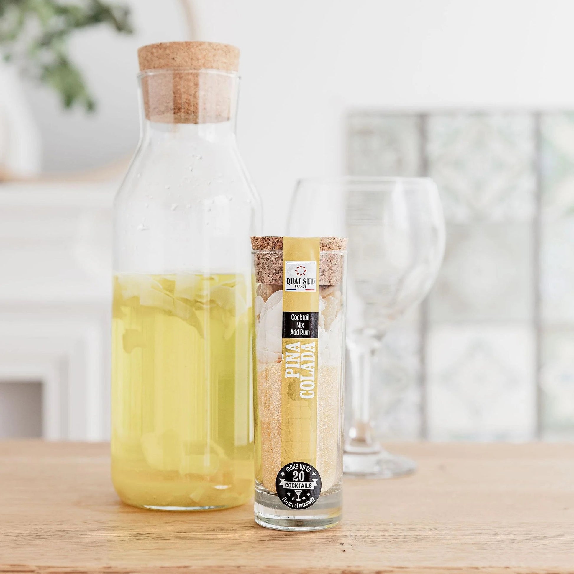 Piña Colada cocktail mix beside an infused rum jug and empty glassware on a wooden table.