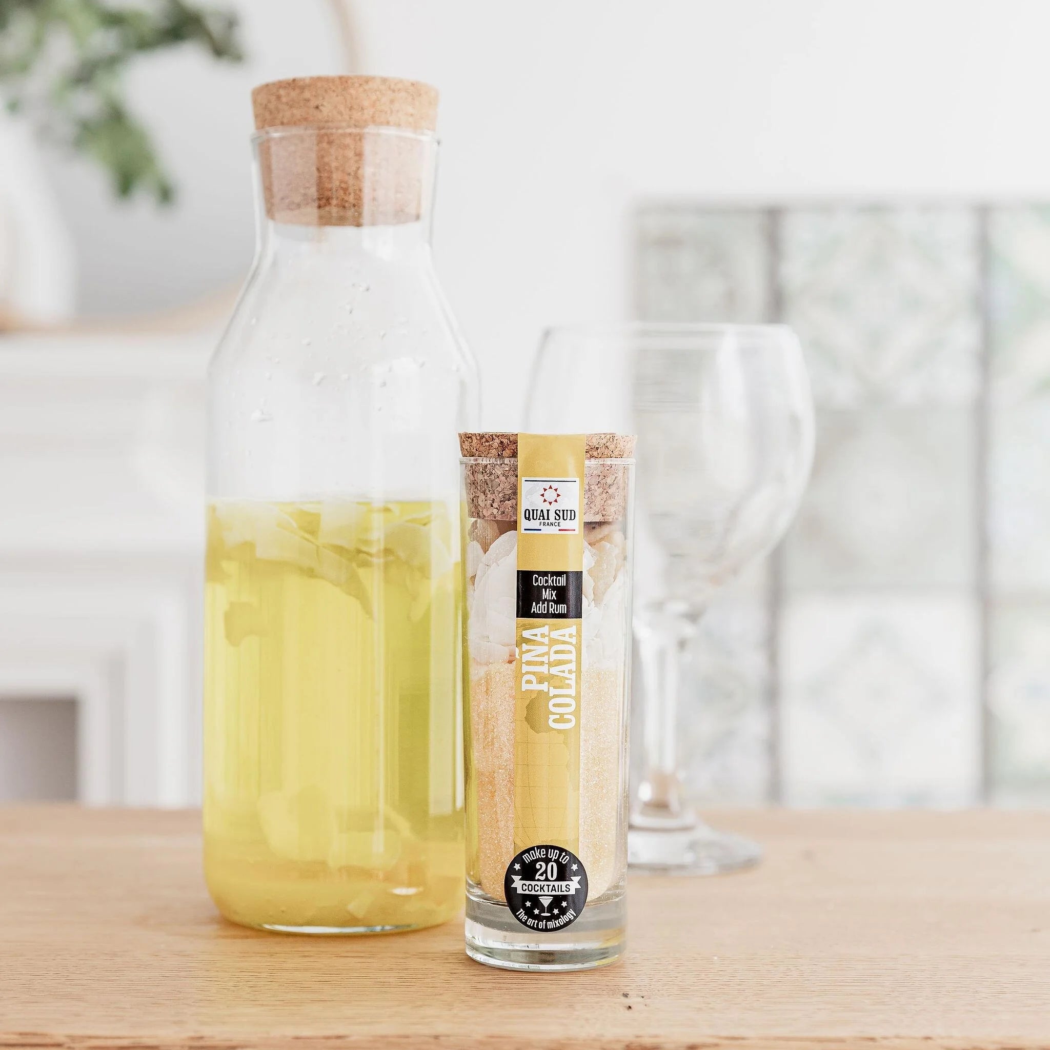 Piña Colada cocktail mix beside an infused rum jug and empty glassware on a wooden table.