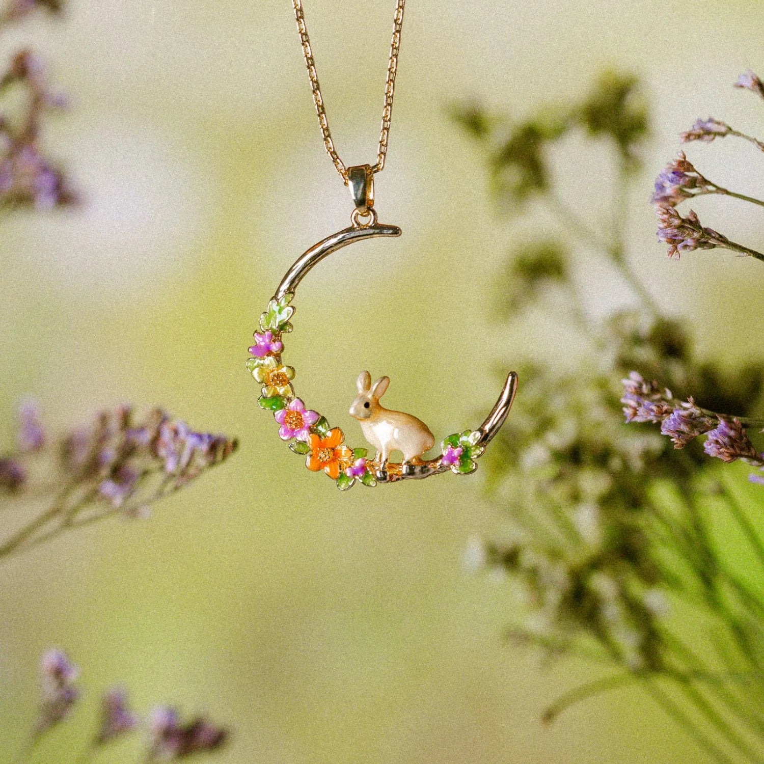 Rabbit Hoop Necklace hanging among flowers, highlighting gold and pastel tones.