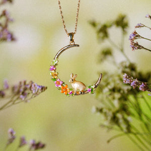  Rabbit Hoop Necklace hanging among flowers, highlighting gold and pastel tones. 