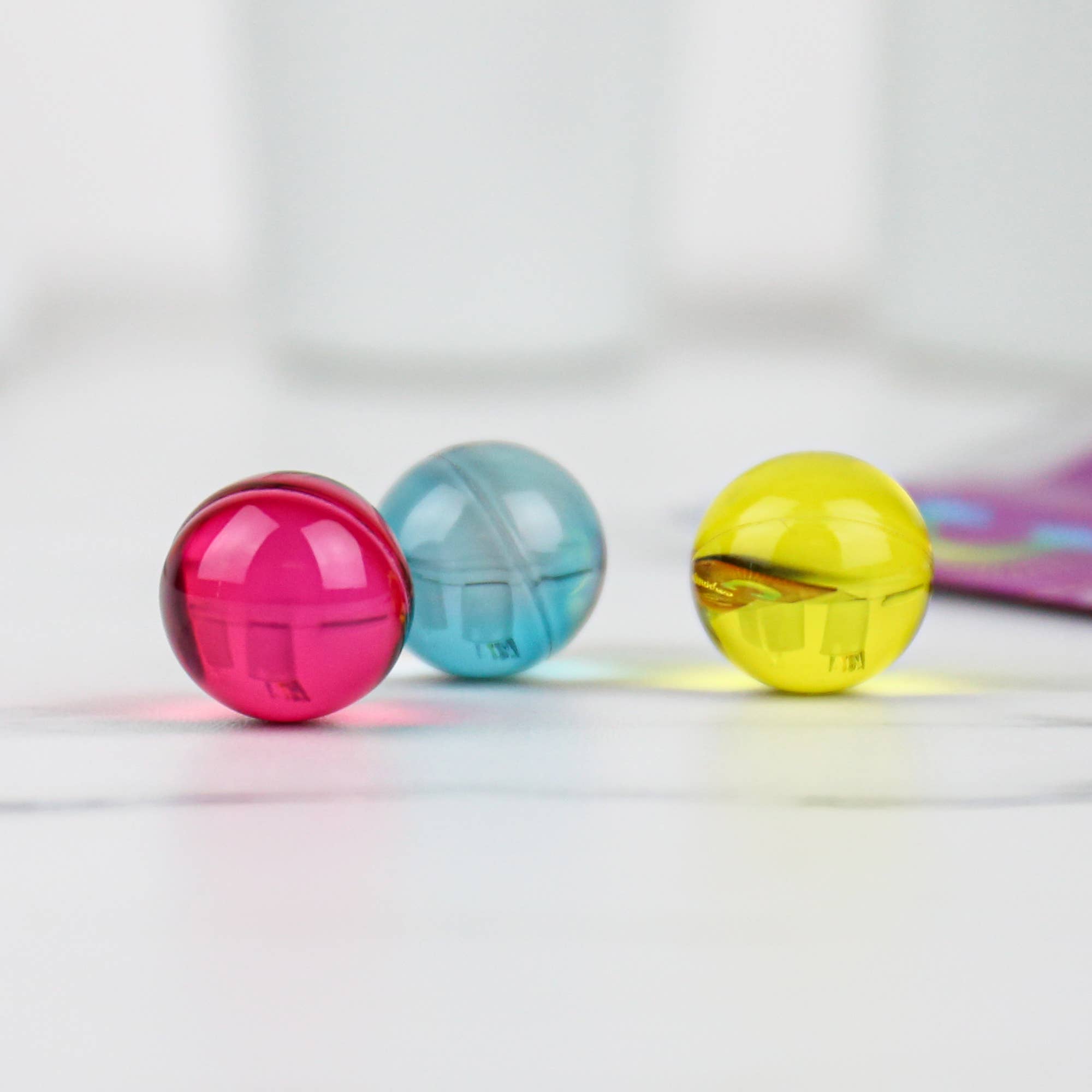 Close up of pink, blue, and yellow rainbow bath pearls on a white surface.