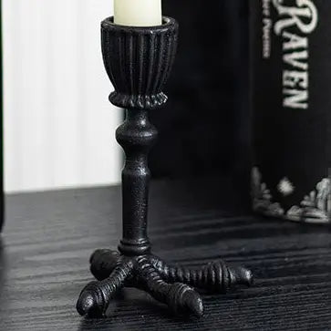 Raven claw gothic candle holder with lit taper candle in dark setting