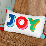 Joy embroidered cushion with pom poms on wicker chair