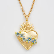 Gold sacred heart necklace with blue floral pendant on white background.