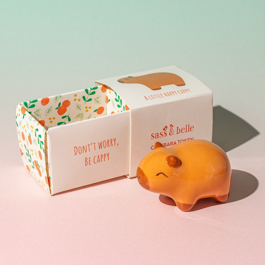 Capybara ceramic token with open illustrated gift box on pink background