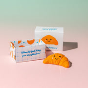 Croissant token beside open gift box on pink and green gradient background