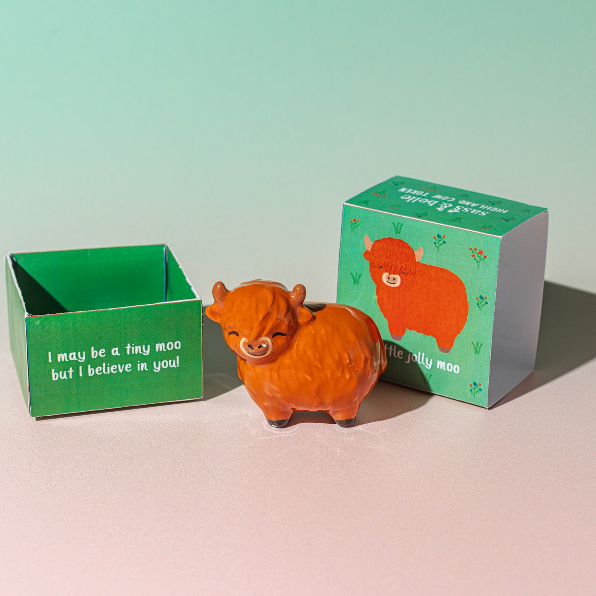 Highland cow token with open green illustrated gift box on pink background