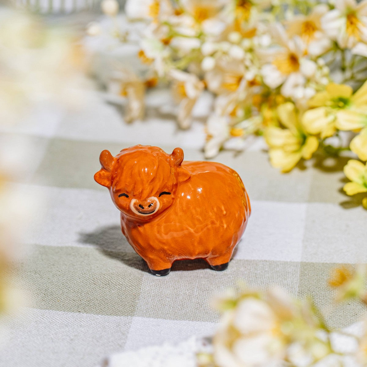Highland cow ceramic token on gingham tablecloth with yellow flowers