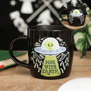 Black mug with alien design on dark background with plants