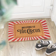 Doormat on wooden floor showing circus tent design with shoes