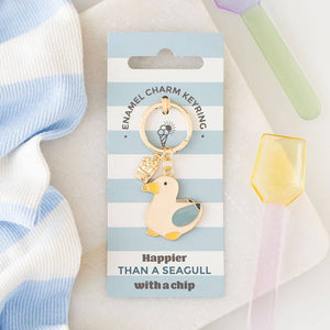 Seagull and Chips enamel keyring on striped blue and white background, featuring gold-tone seagull charm with chip detail and beach-inspired packaging.