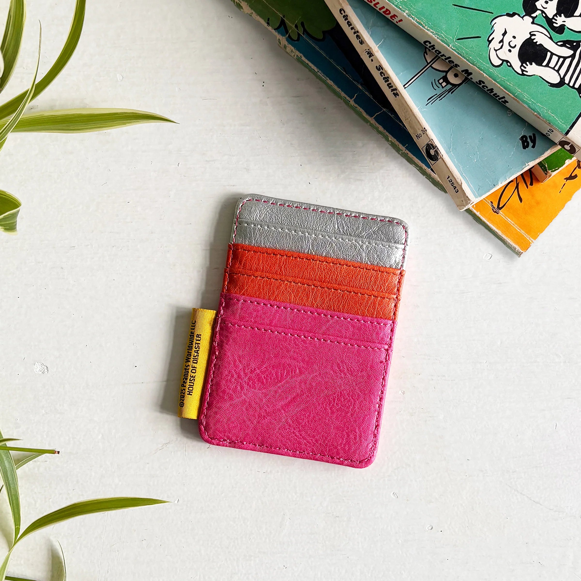 Peanuts Rockstar Cardholder back side on white surface with comic books and green leaves.