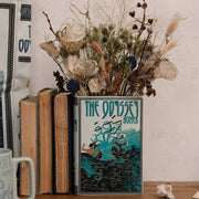 The Odyssey book vase holding dried flowers on a wooden surface
