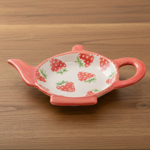 Strawberry teapot-shaped teabag rest dish in red with green leaf detail on white background