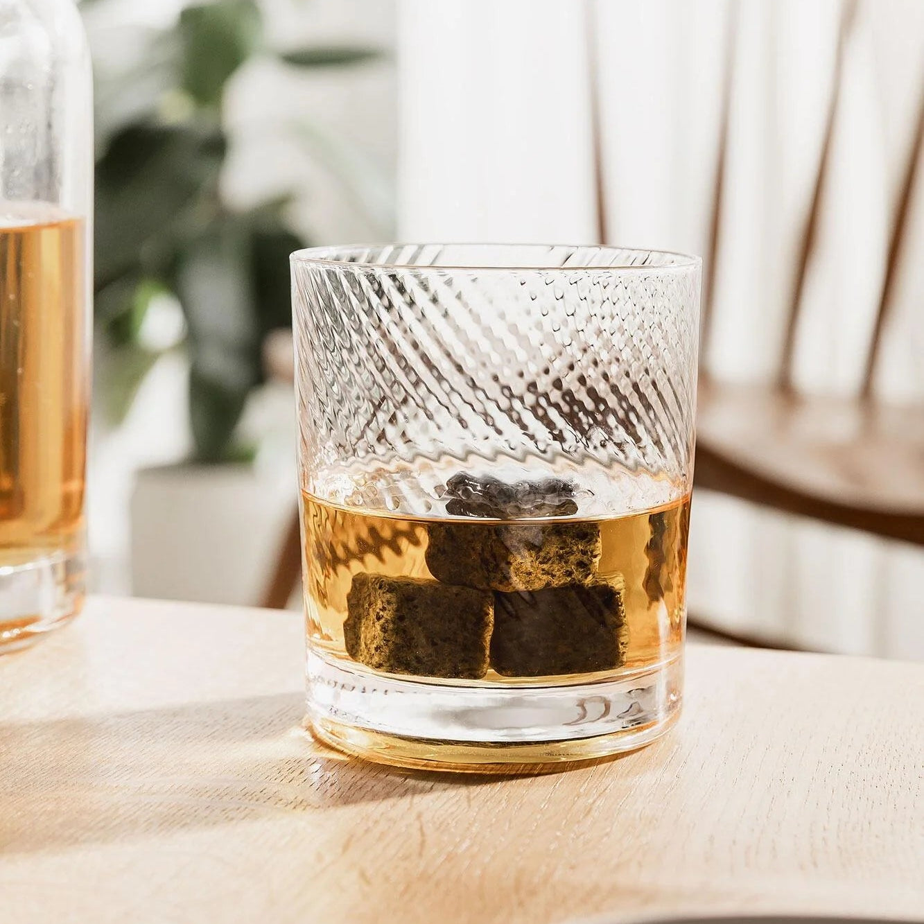 Twisted Whiskey Glass filled with whisky and whisky stones on wooden table.
