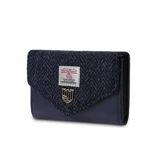 A Harris Tweed navy blue herringbone purse from the side, showcasing the intricate herringbone pattern and the golden popper closure. The fabric is handwoven in the Outer Hebrides of Scotland, making each purse unique and of the highest quality.