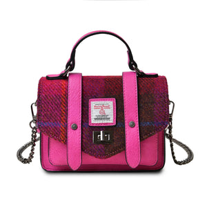 Harris Tweed mini satchel style handbag. It is finished in red and pink PU leather and has a Red Tartan Harris Tweed fabric. The shoulder strap is draped over the back of the bag. 