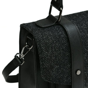 The Islander Black Herringbone Harris Tweed Satchel style handbag from the left handside showing a close up of the removable shoulder strap and the Black Herringbone fabric. 